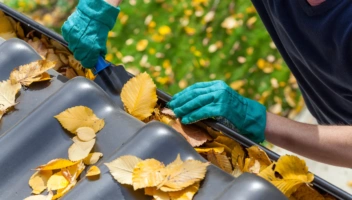 Homeowner cleaning fall leaves from gutter