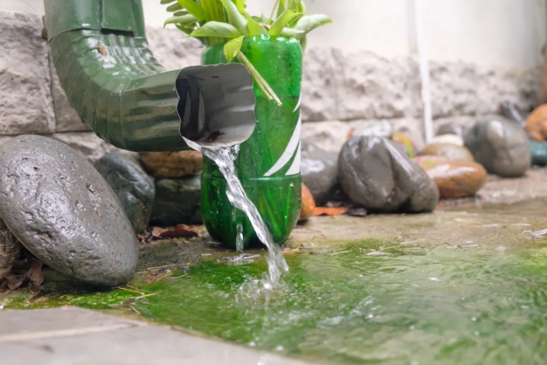 Green downspout with water cascading onto rocks.