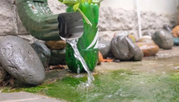 Green downspout with water cascading onto rocks.